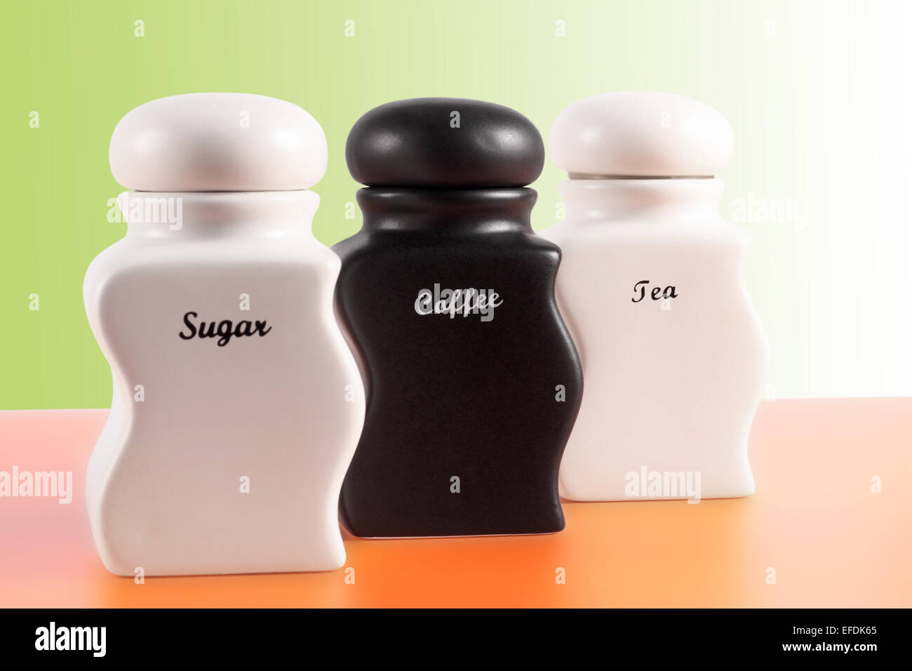 Capacità di zucchero, caffè, tè su una superficie di colore arancione e uno sfondo verde. Foto Stock