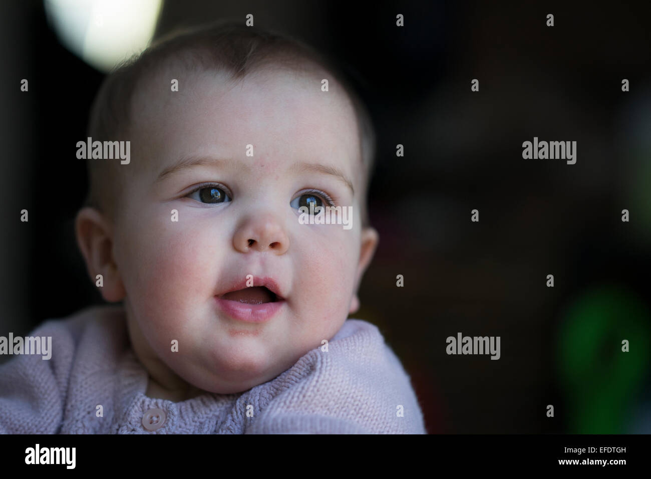 A dieci mesi di età Baby girl il peering fuori della finestra mentre si sta giocando con i suoi giocattoli. Foto Tim Clayton Foto Stock