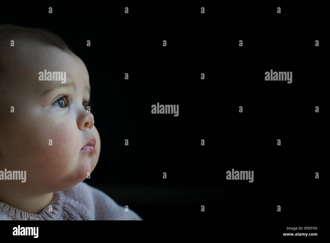 A dieci mesi di età Baby girl il peering fuori della finestra mentre si sta giocando con i suoi giocattoli. Foto Tim Clayton Foto Stock