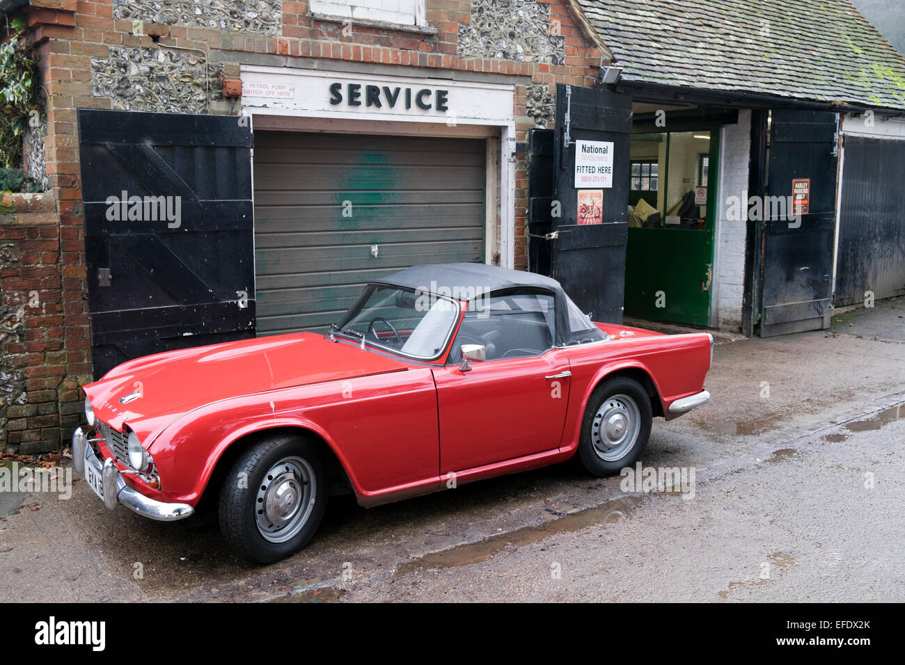 Trionfo TR4 un rosso British classic sport auto parcheggiate al di fuori di un garage nel villaggio di Hambleden Buckinghamshire REGNO UNITO Foto Stock