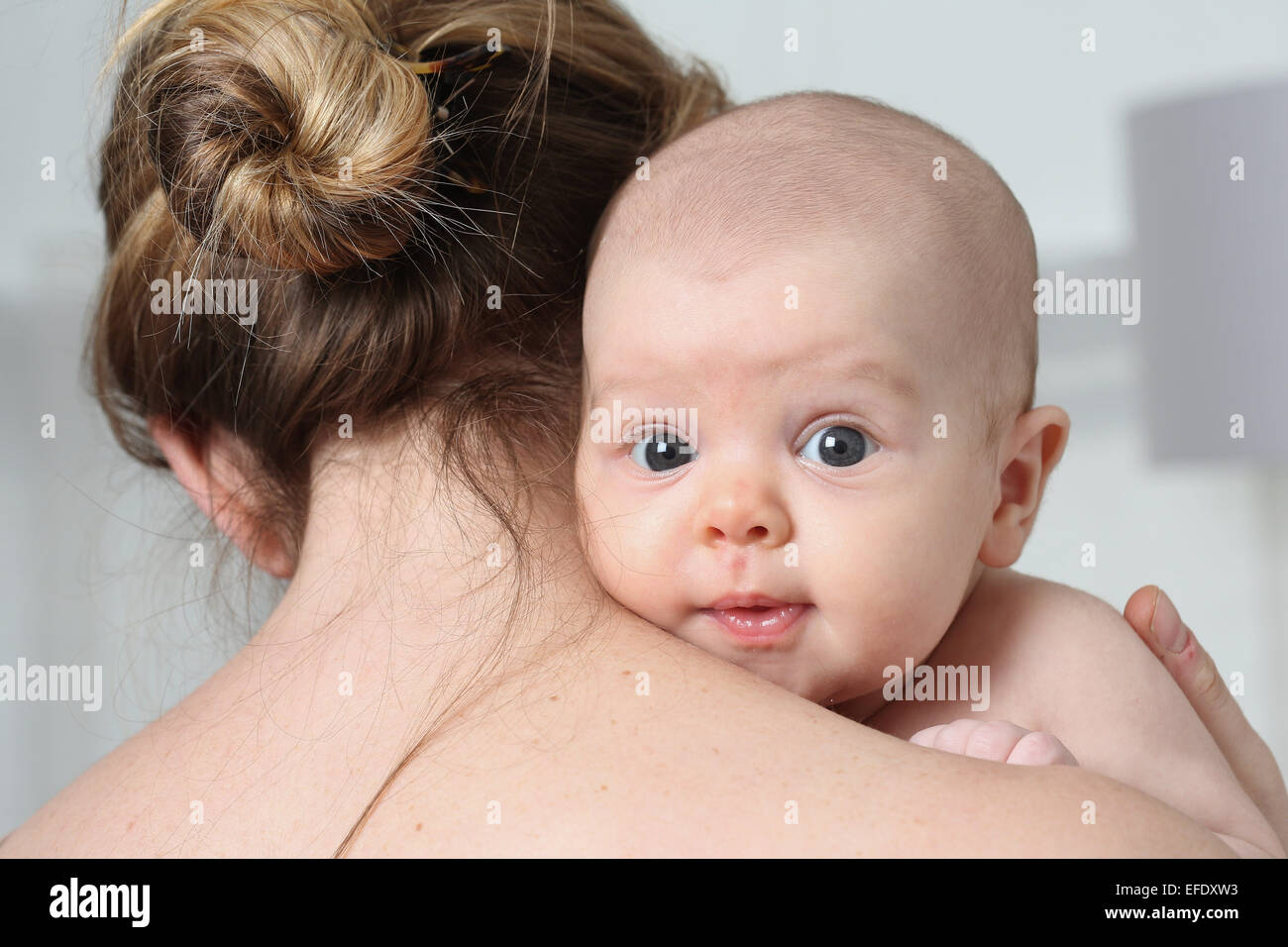 Un mese due vecchi bambina in una camera da letto si appoggia sulla sua spalla madri mentre si effettua il contatto visivo con la telecamera. Foto Tim Clayton Foto Stock