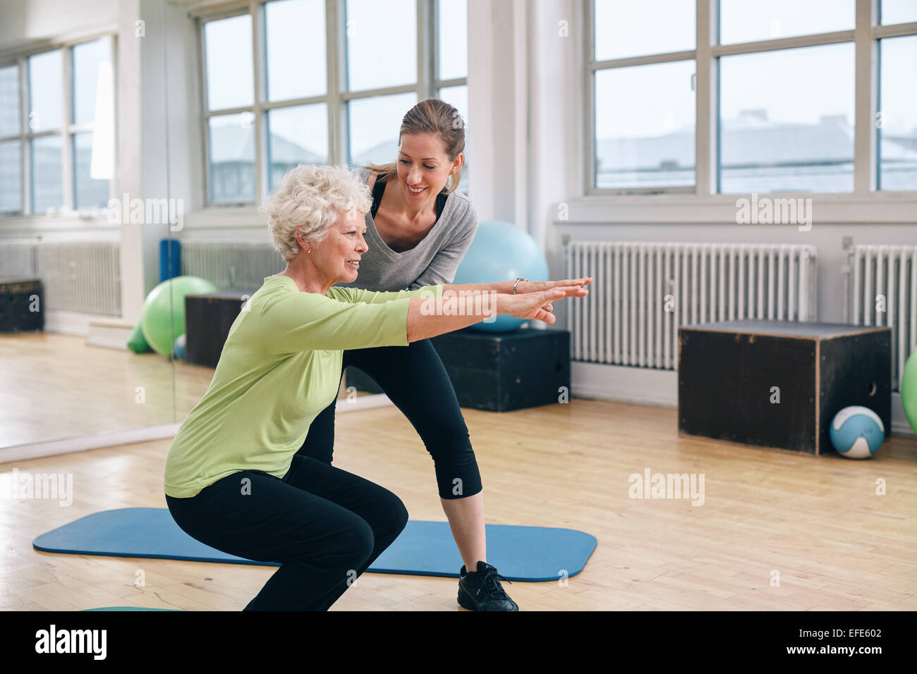 Donna anziana fare esercizio con il suo personal trainer presso la palestra. Istruttore di palestra assistere senior donna nel suo allenamento. Foto Stock