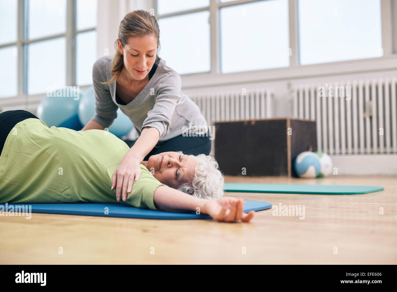 Le donne anziane che giace sul tappeto di esercizio facendo stretching allenamento per i muscoli della schiena con pullman assistenza. Trainer femminile aiutando il sambuco Foto Stock