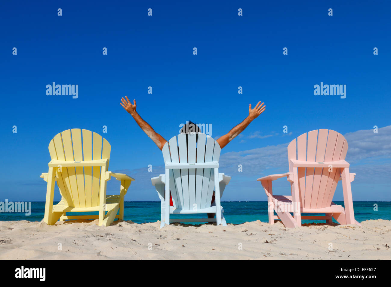 Uomo con le mani in aria posti a sedere sulla sedia colorata sulla spiaggia Caraibica Foto Stock