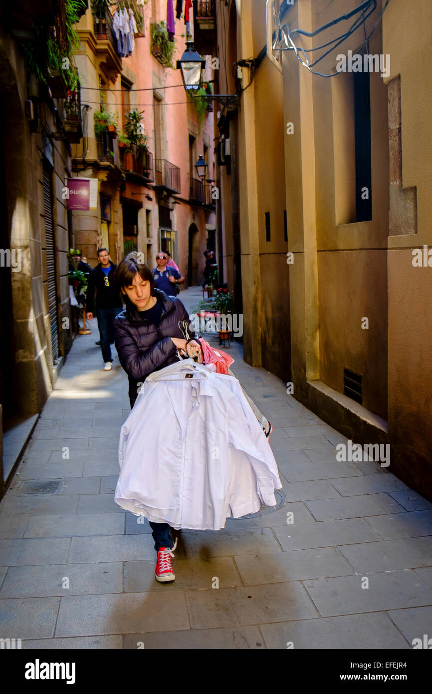 Giovane ragazza che porta una pila di magliette su staffe attraverso una strada sul retro vicino a La Rambla di Barcellona, Spagna Foto Stock
