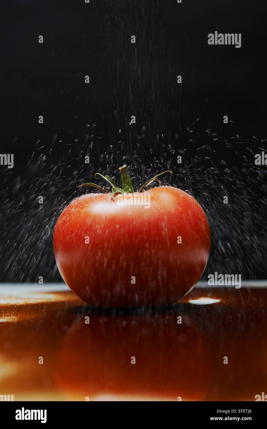 Il pomodoro con il sale che cade su di esso seduti in un pool di aceto balsamico. Fotografia di cibo Foto Stock