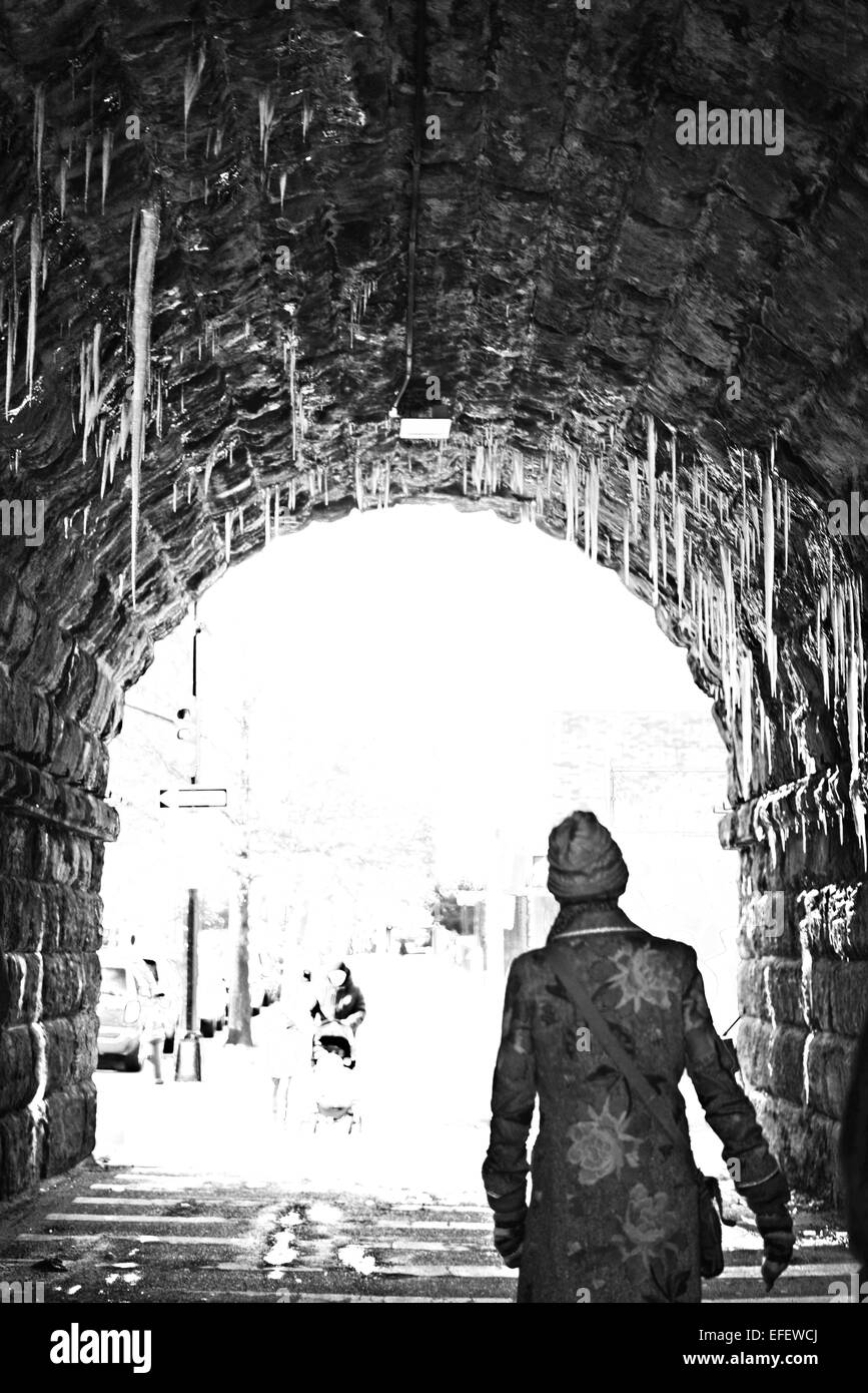Le donne a piedi attraverso un tunnel con ghiaccioli che pendono in BW in inverno Foto Stock