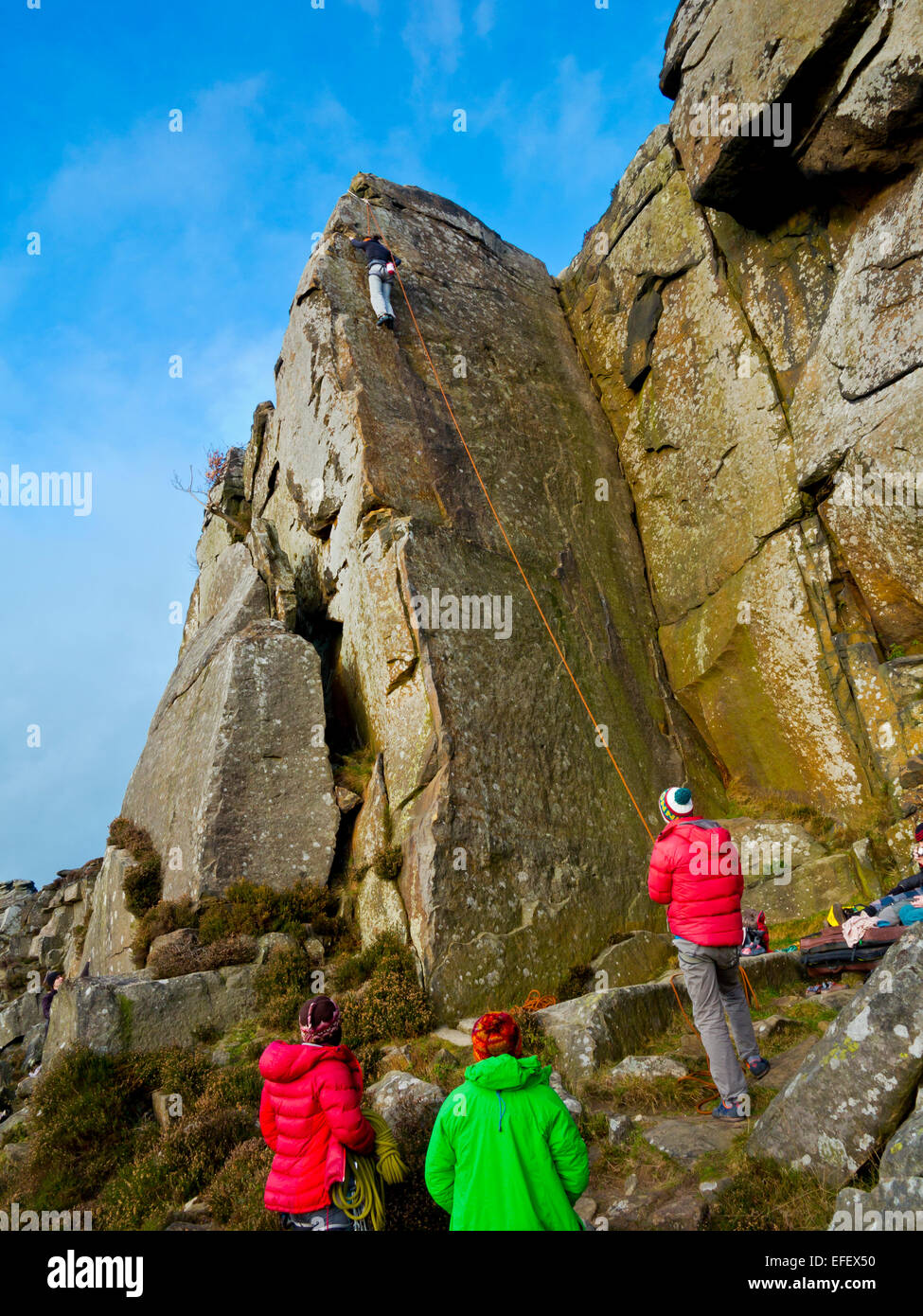 Un gruppo di alpinisti di guardare un amico salendo una ripida scogliera faccia su rocce al bordo Curbar Parco Nazionale di Peak District DERBYSHIRE REGNO UNITO Foto Stock