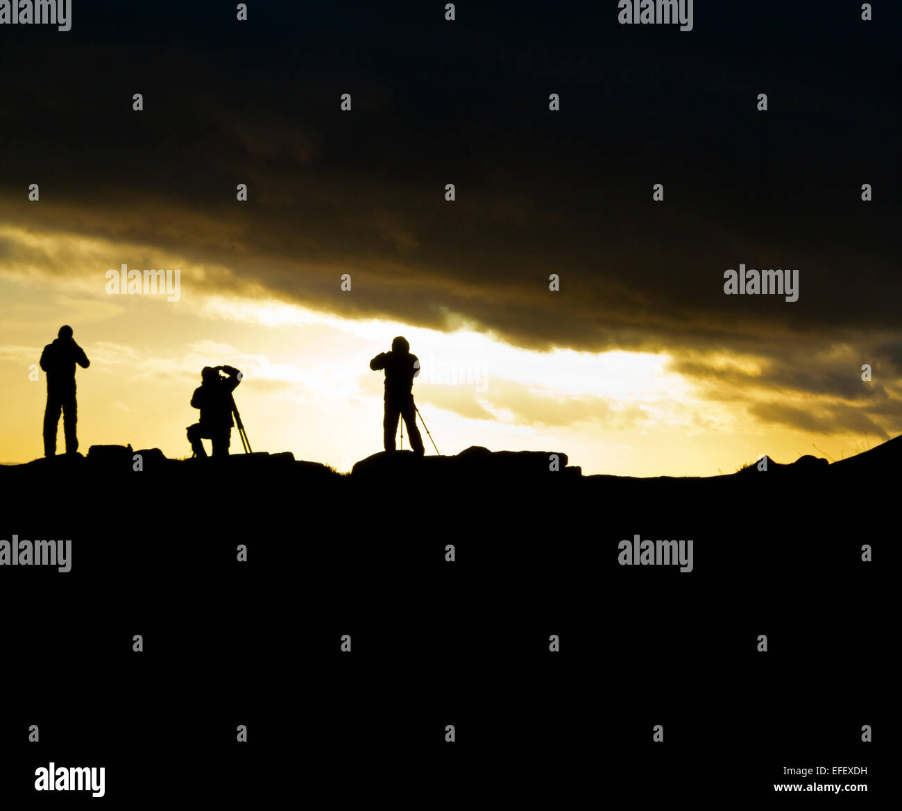 Il gruppo di fotografi con treppiedi stagliano contro il tramonto a bordo Curbar nel Parco Nazionale di Peak District DERBYSHIRE REGNO UNITO Foto Stock