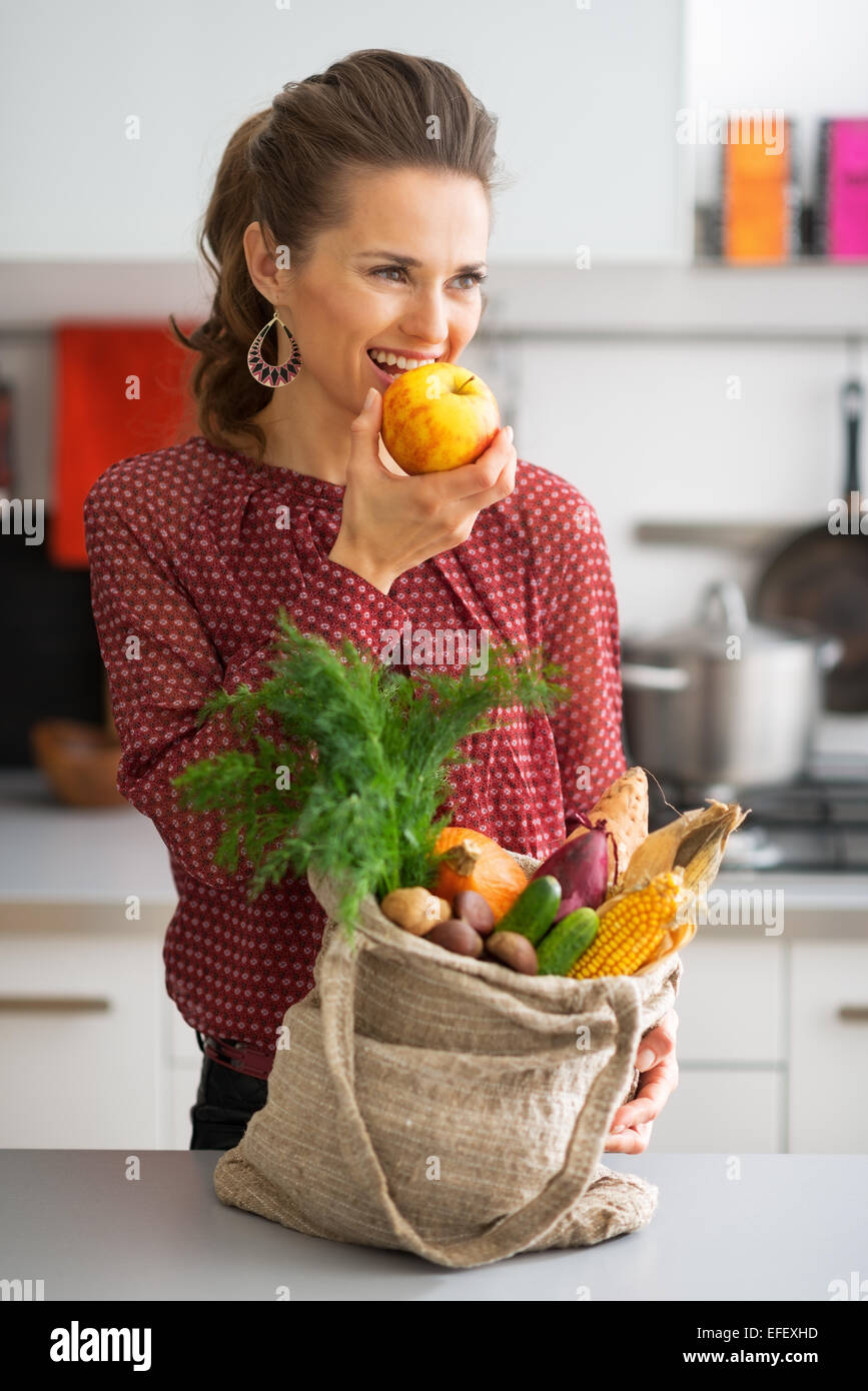 Giovani casalinga con gli acquisti dal mercato locale mangiando apple Foto Stock