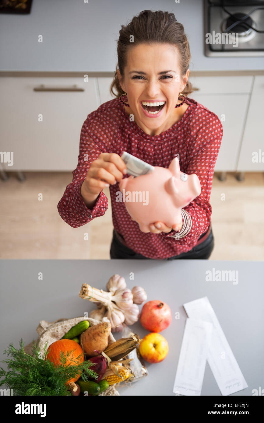 Felice giovane massaia mettere soldi nel salvadanaio dopo lo shopping sul mercato locale Foto Stock