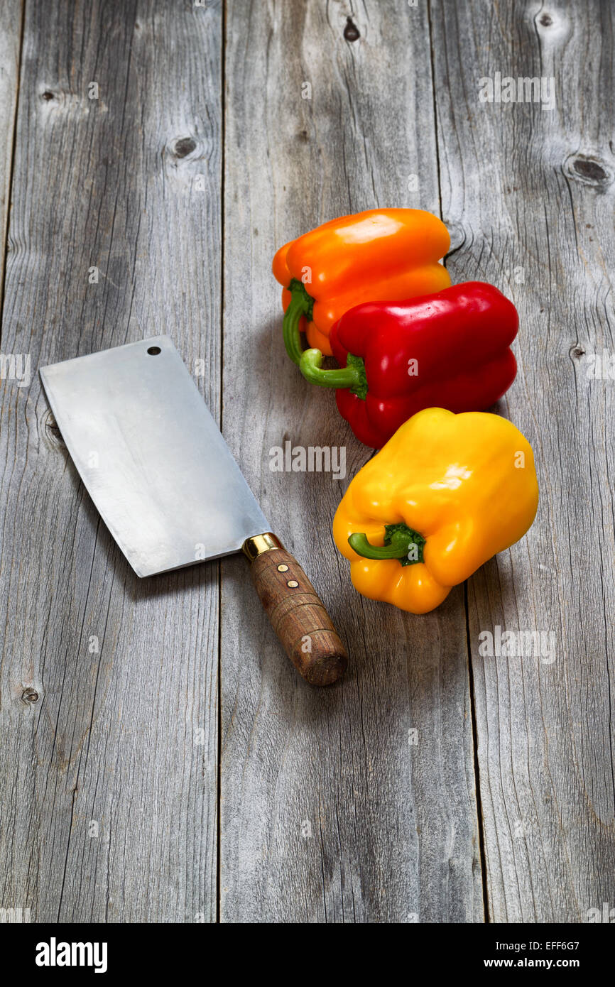 L'immagine verticale di tre nuovi i peperoni e il vecchio coltello da prosciutto su invecchiato schede boschive Foto Stock