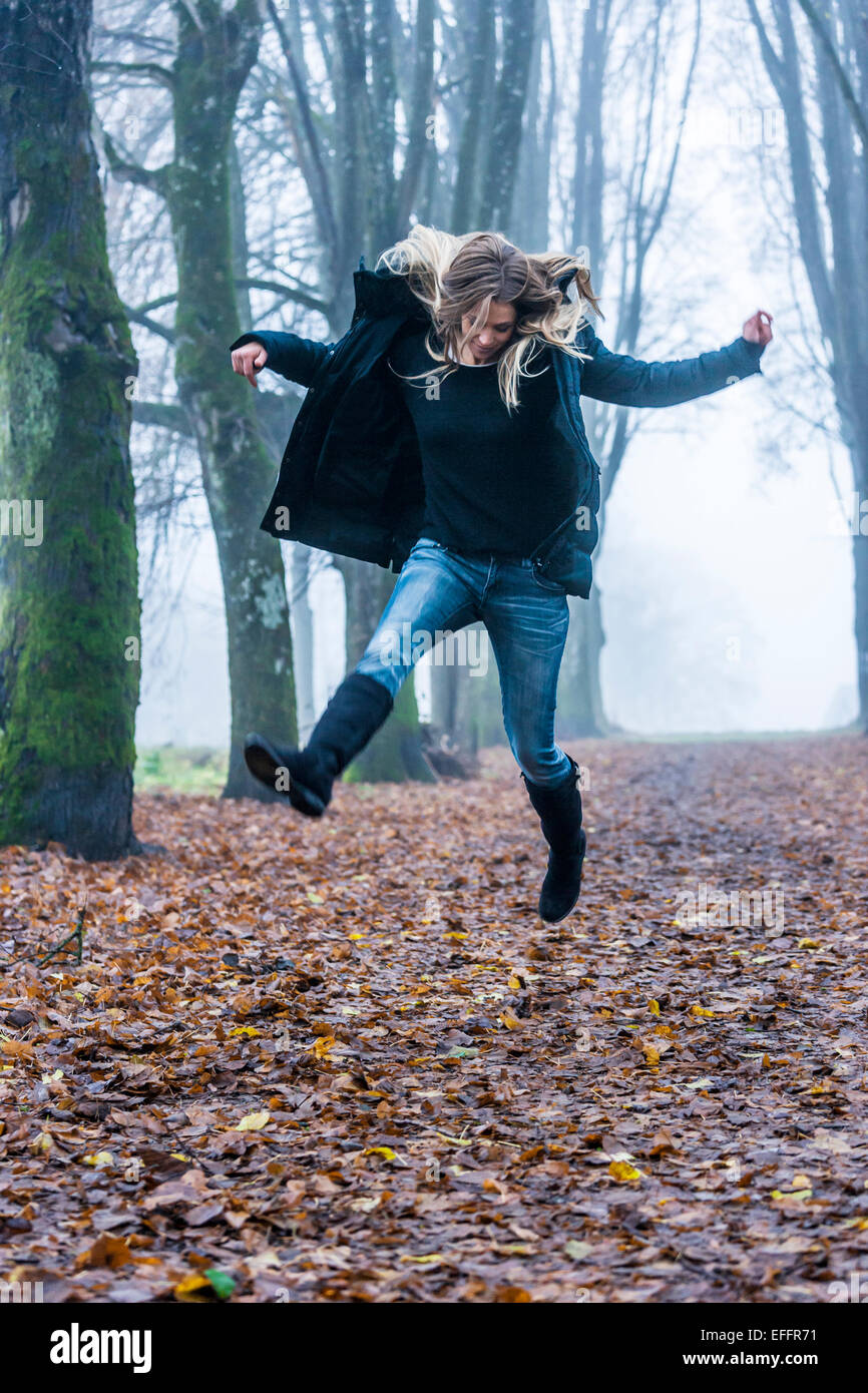 Donna salta in aria su una pista forestale Foto Stock