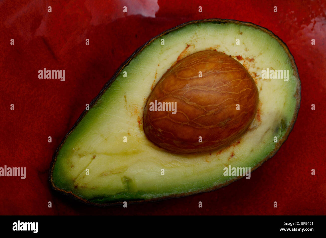 Dolce metà di avocado su un rosso piattino in ceramica Foto Stock