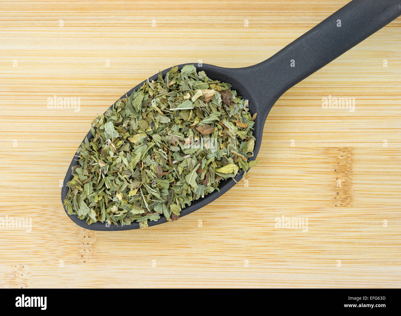 Shredded menta verde foglie di erbe in un cucchiaio di nero su un legno tagliere. Foto Stock