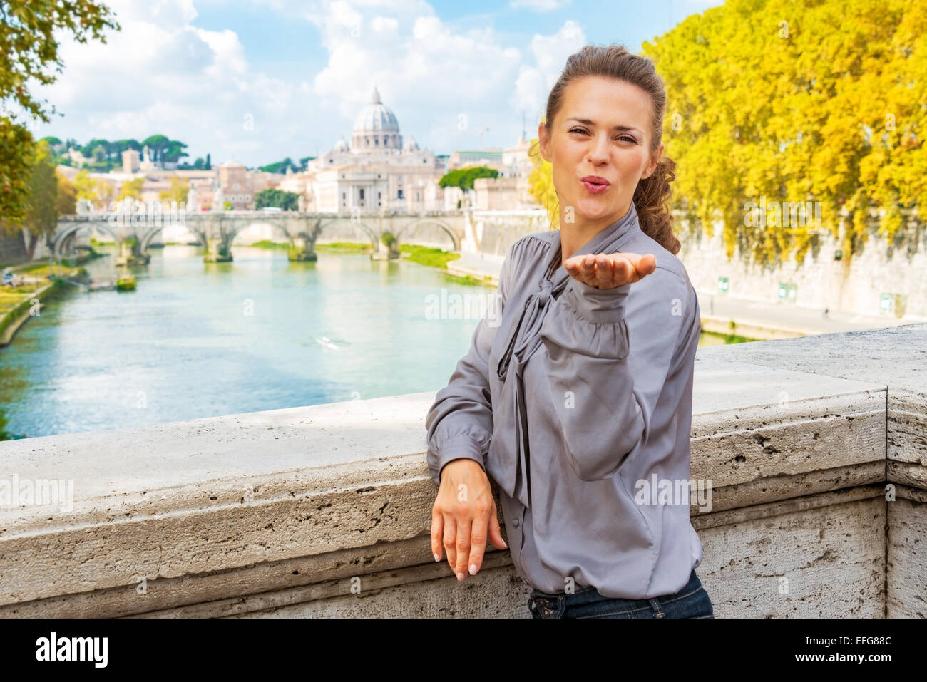 Giovane donna soffiando kiss da Ponte Umberto I con vista sulla basilica di san pietro Foto Stock