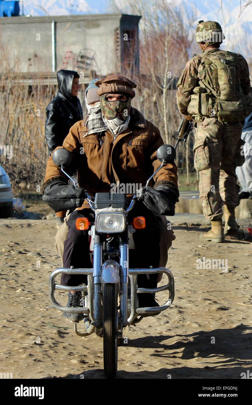 Un uomo afghano cavalca un motociclo passa una pattuglia di americani, ceco e soldati afgani come essi patrol attraverso un villaggio 27 gennaio 2015 nella provincia di Parwan, Afghanistan. Foto Stock