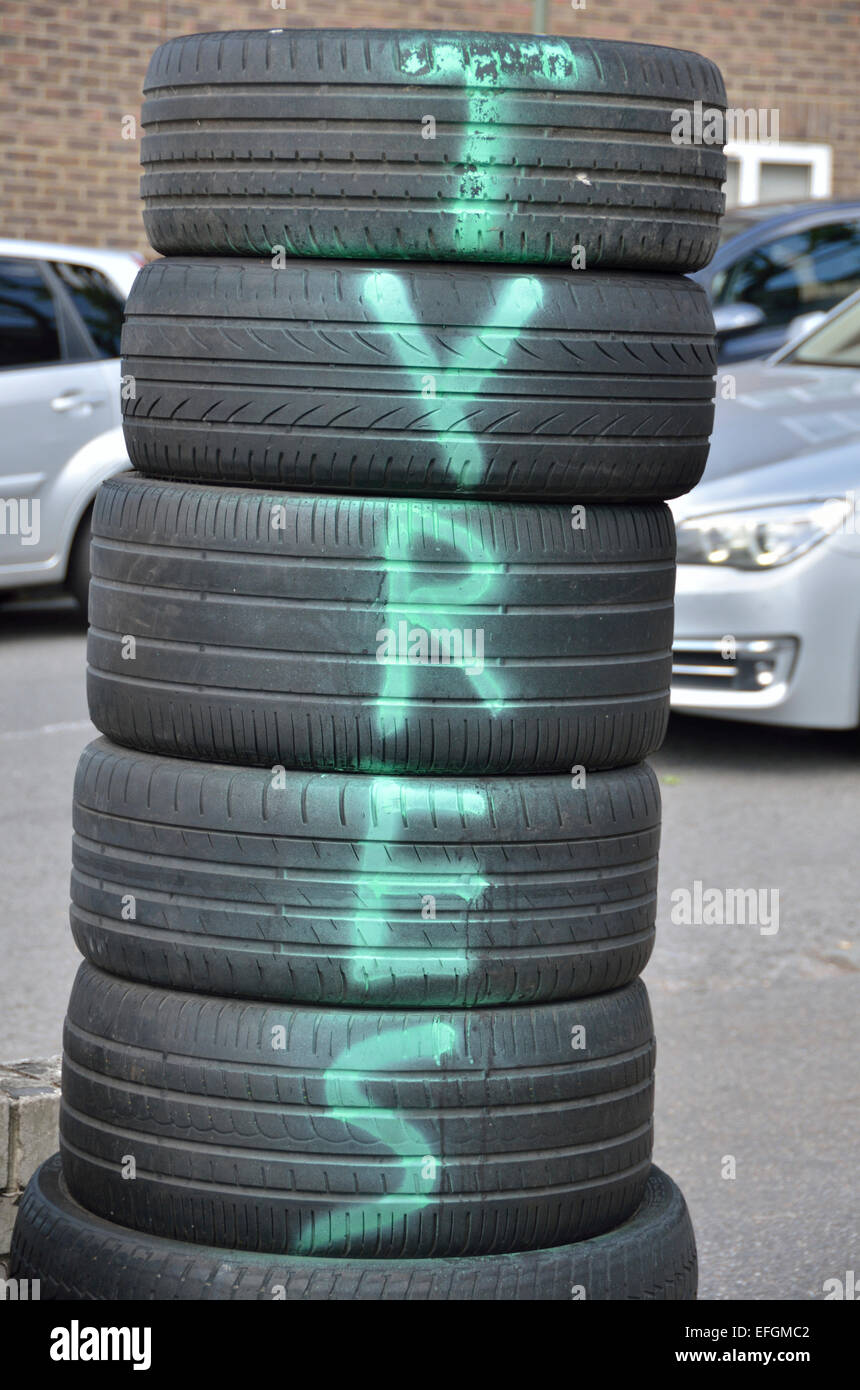 La parola " PNEUMATICI " spruzzato su una pila di pneumatici per auto al di fuori di un garage Foto Stock
