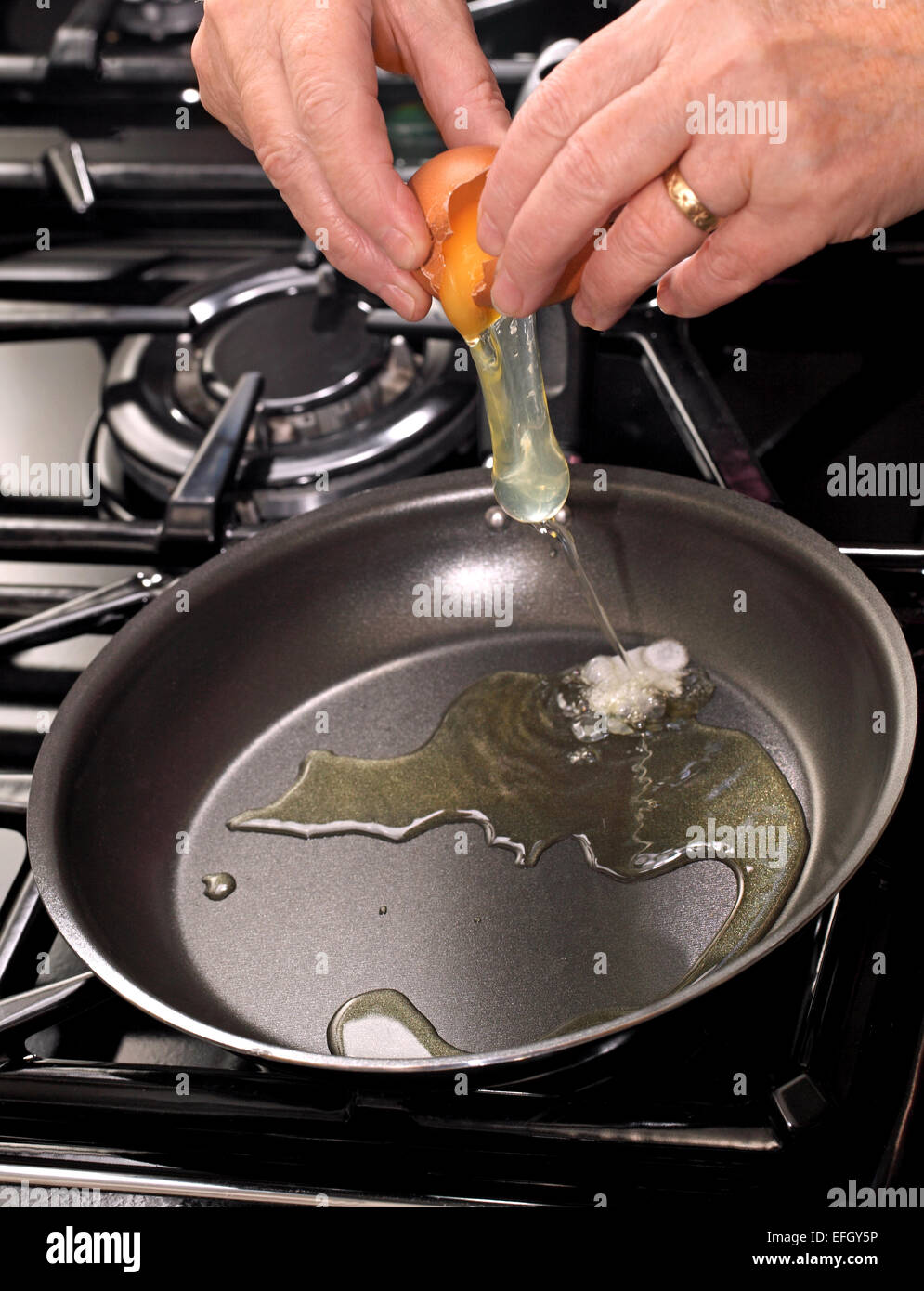 Una donna di cracking di aprire un uovo in una padella su un piano cottura a gas Foto Stock