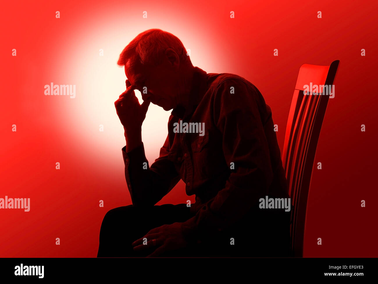 Spot sfondo illuminato dando un effetto di silhouette di un uomo di circa 60 anni che è seduto su una sedia guardando preoccupato, malati o stanchi. Foto Stock