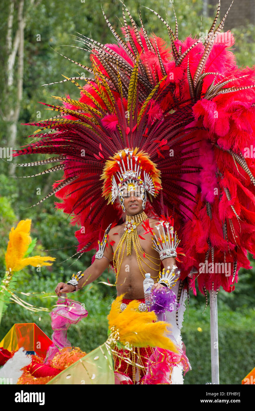 Carnevale maschio performer che indossa un elaborato copricapo di piume di colore rosso su un galleggiante in processione, il carnevale di Notting Hill, London, England, Regno Unito Foto Stock