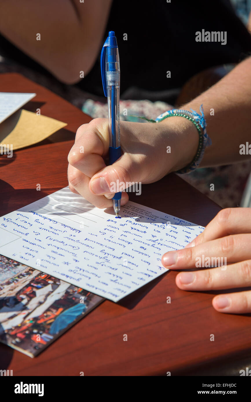 Le mani della ragazza cartolina di scrittura a un tavolo nella luce solare Foto Stock