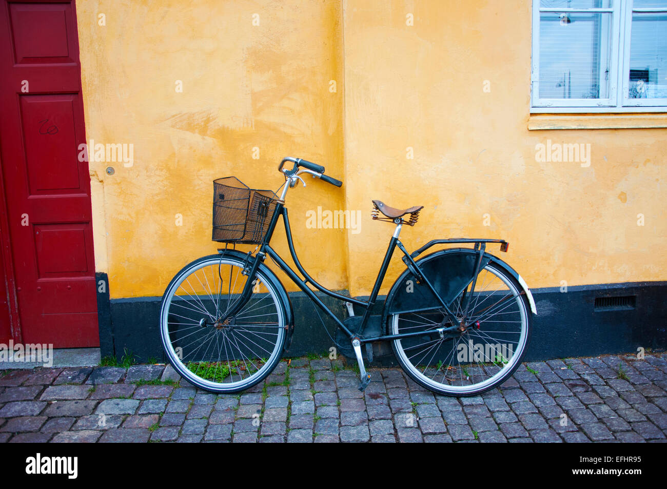 Un unico moto con un cestello poggia contro una luminosa parete gialla che illustra Copenhagen Danimarca la romantica bike cultura. Foto Stock