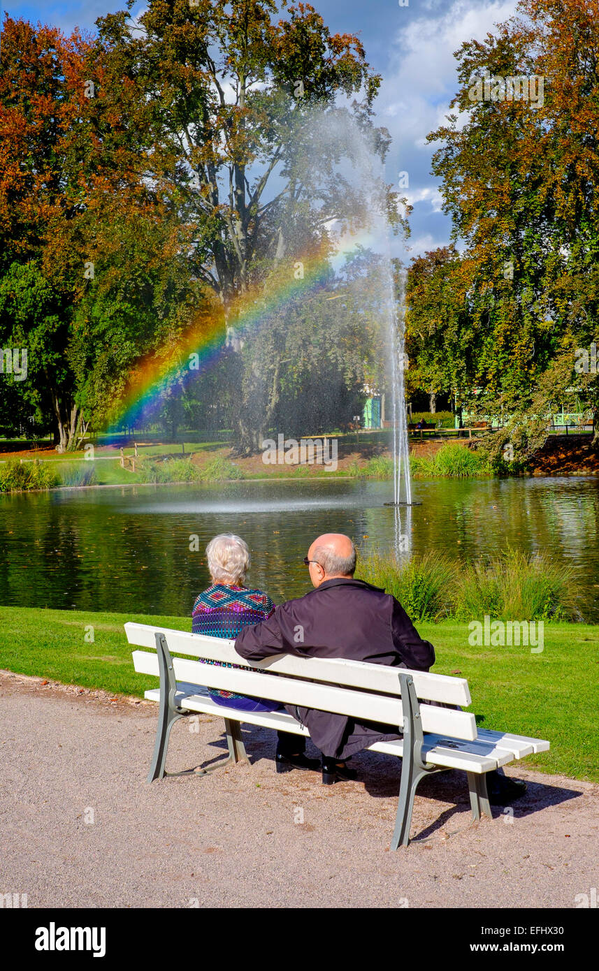 Coppia di anziani sul banco, getto di acqua con arcobaleno, Parc de l'Orangerie park, Strasburgo, Alsazia, Francia, Europa Foto Stock