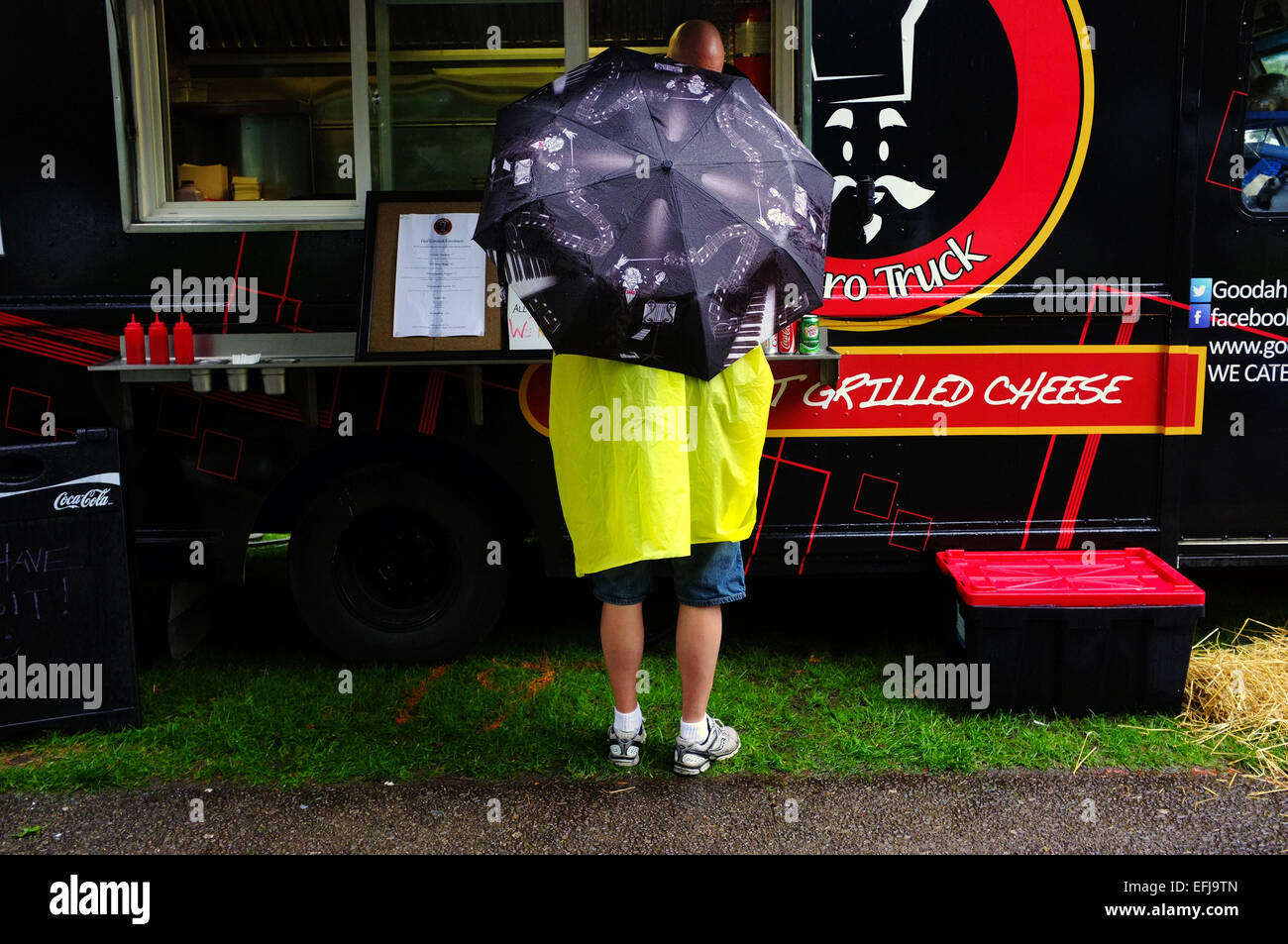 Una persona in piedi sotto un ombrello ordini da un alimento van durante un festival. Foto Stock