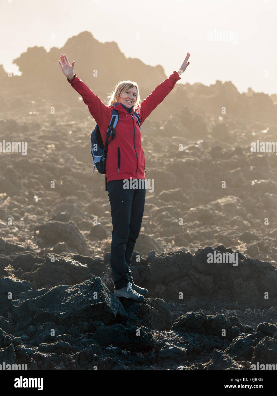 Donna sorridente con mani aperte in piedi vicino alla cima del vulcano Foto Stock