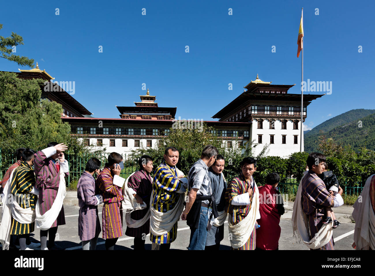 Il Bhutan - uomini della linea aspettando pazientemente in abito tradizionale, (ghos), che passa attraverso il punto di controllo di sicurezza per il festival. Foto Stock