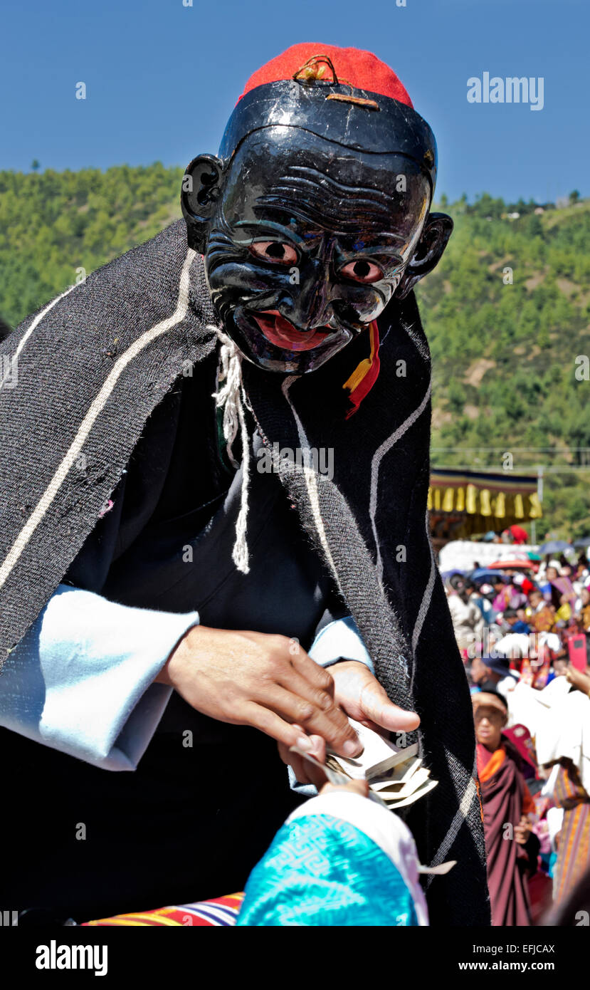 Il Bhutan - spettatori dare i soldi per i clown che cavort intorno alla più grave di ballerini in tutta la loro lunga le prestazioni. Foto Stock