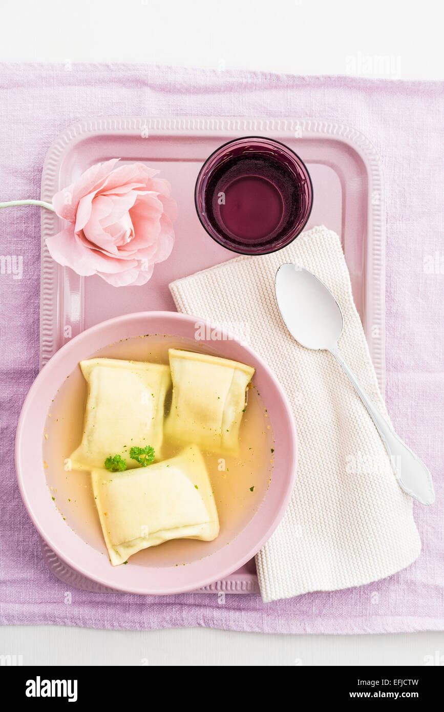 Maultaschen riempito quadratini di pasta in brodo con acqua e una carta crespa fiore su un vassoio Foto Stock
