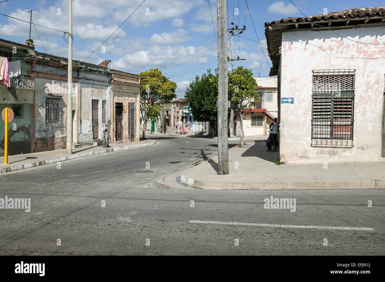 Strada residenziale e angolo con tetto piatto weathered stucco case, una strada a freccia e cubani locali sul marciapiede, Cienfuegos, Cuba. Foto Stock