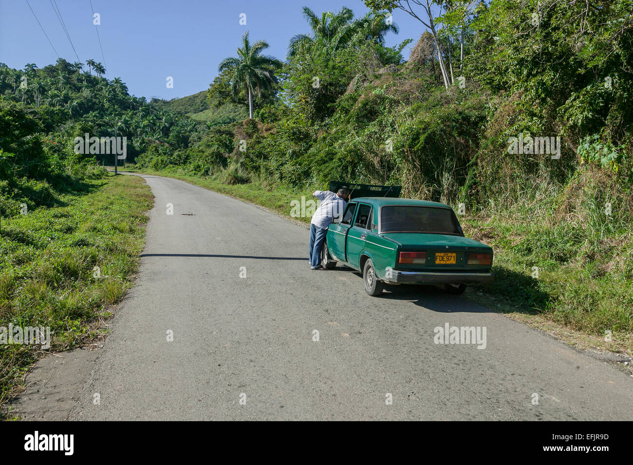 Uomo cubano con problemi con la macchina sollevando il cofano della sua auto su un solitario strada deserta nelle montagne Escambray a Cienfuegos, Cuba Foto Stock