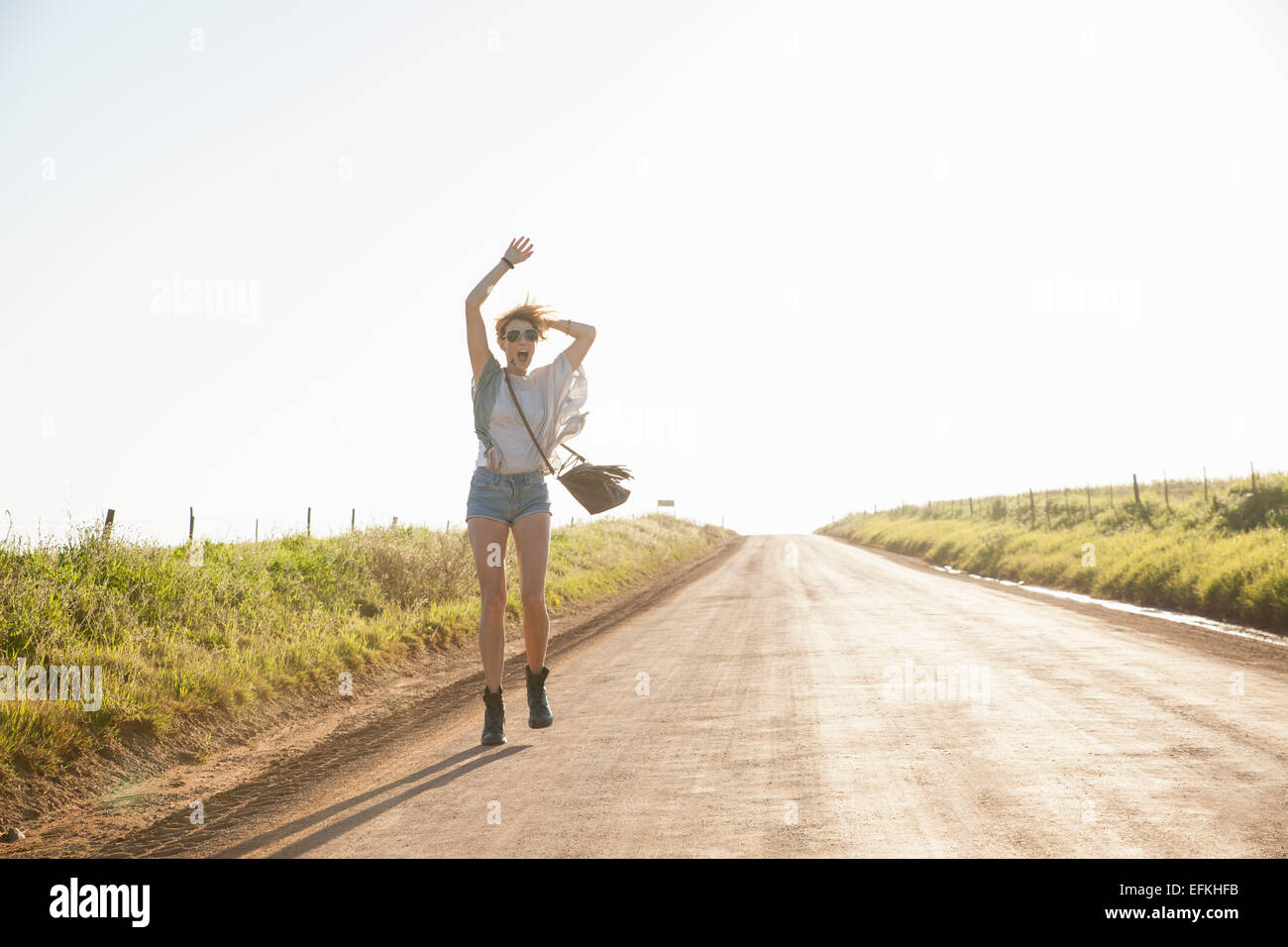 Metà donna adulta camminando sulla strada di campagna, agitando le braccia in aria Foto Stock Metà donna adulta camminando sulla strada di campagna, agitando le braccia in aria Foto Stock