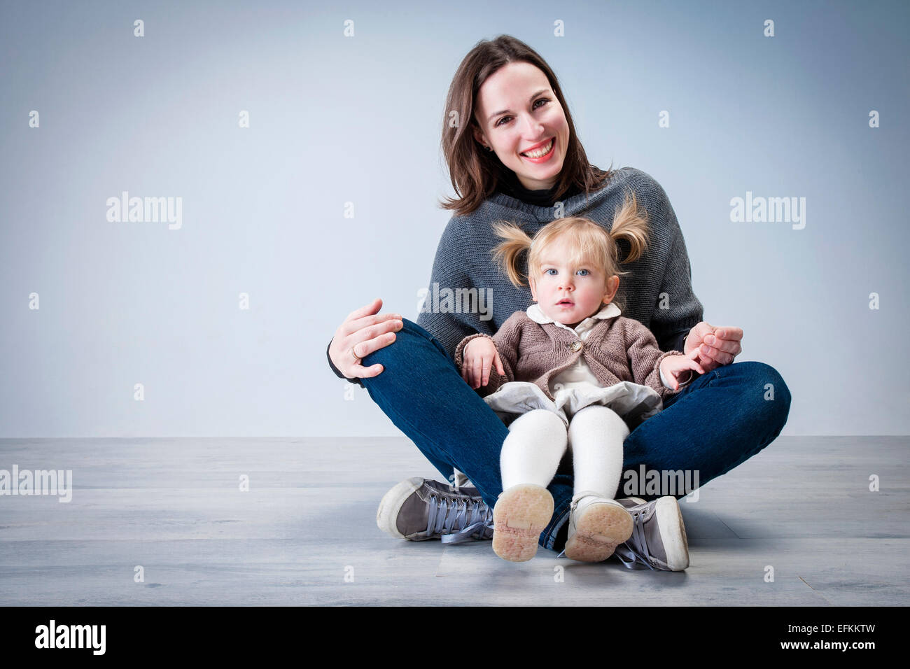 Ritratto di metà donna adulta seduta sul pavimento con la figlia dei bimbi seduti sul giro Foto Stock