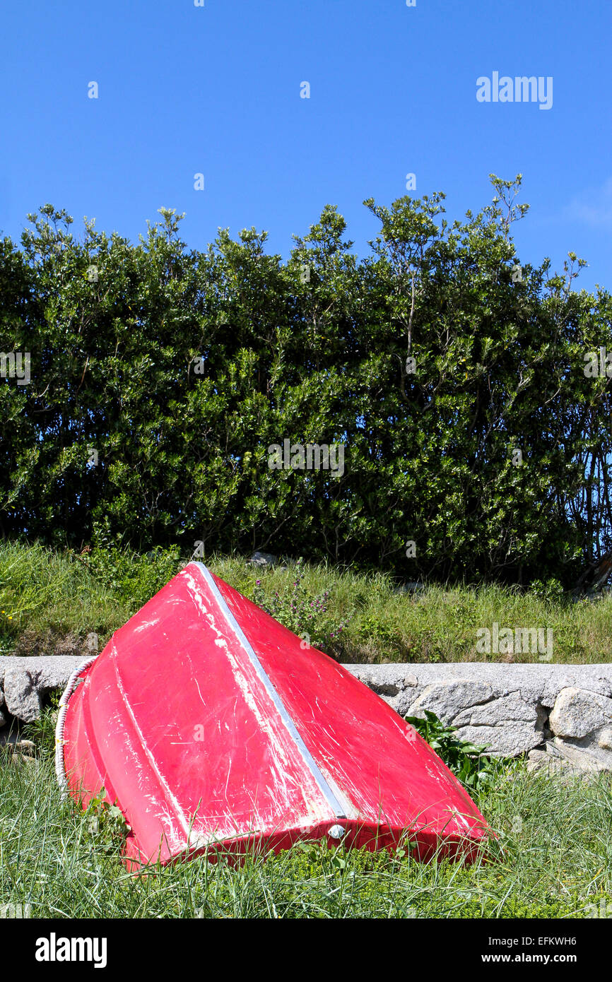 Rosso capovolta barca a remi appoggiata contro il sentiero, isole Scilly, Regno Unito Foto Stock