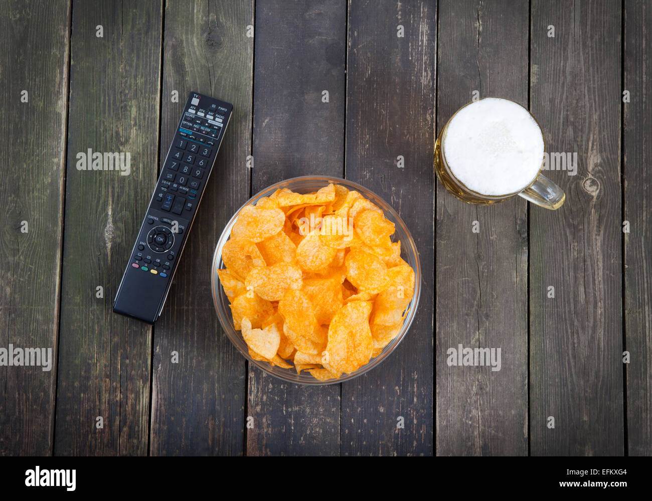 Una ciotola di patatine con un bicchiere di birra e telecomando Foto Stock