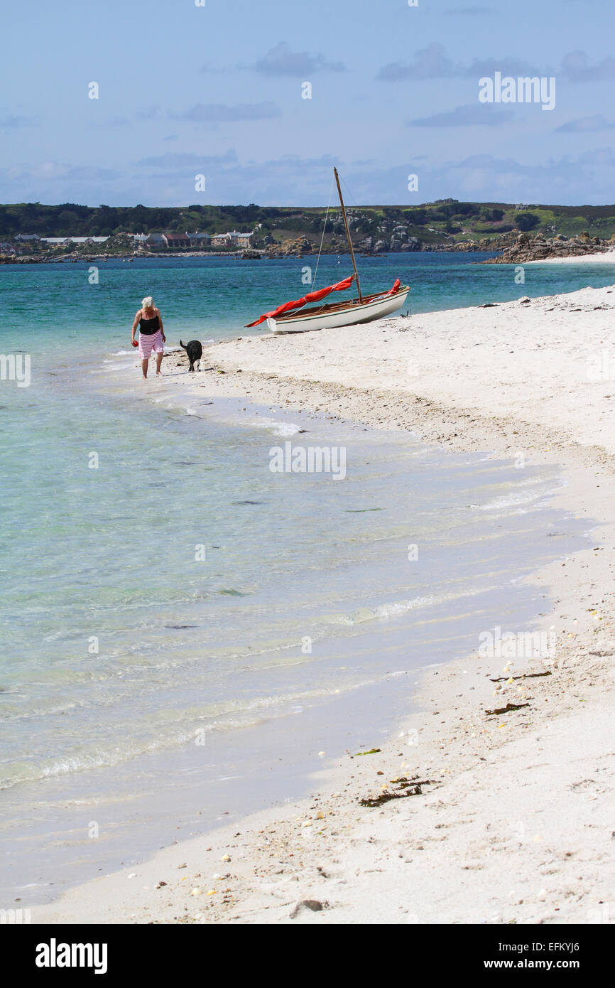 Donna e cane passeggiando a bordo d'acqua sulla spiaggia sabbiosa, isole Scilly, Regno Unito Foto Stock