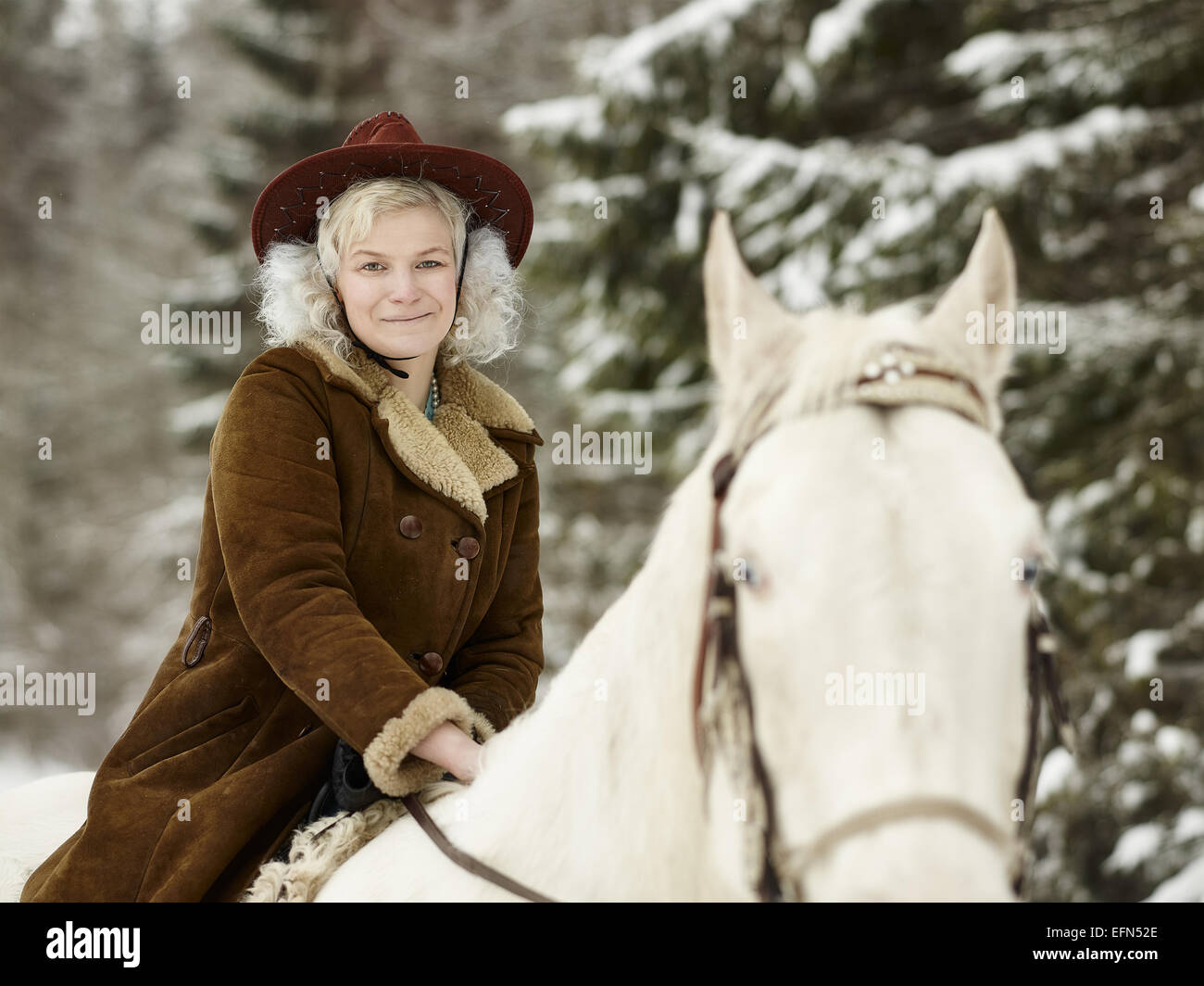 Donna attraente che indossa una giacca invernale e hat, ella in sella ad un cavallo bianco e si guarda verso la telecamera Foto Stock