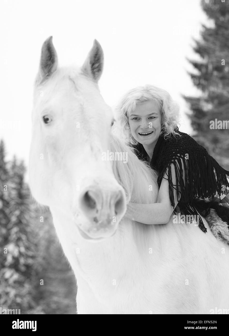 Attraente donna bionda che abbracci un cavallo bianco, coperto giornata invernale Foto Stock