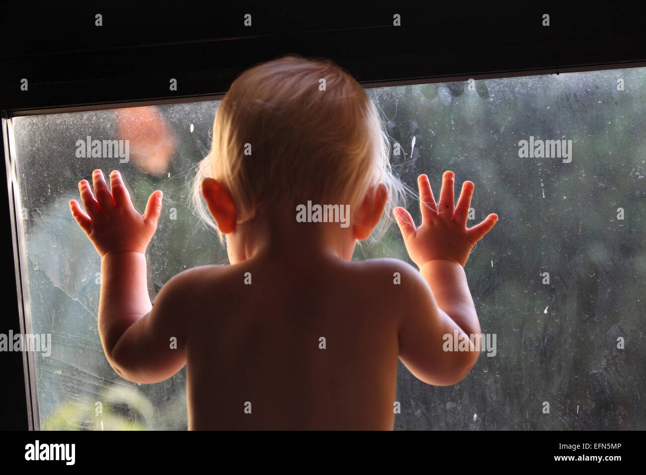 Bambina guarda fuori attraverso una finestra sporca Foto Stock