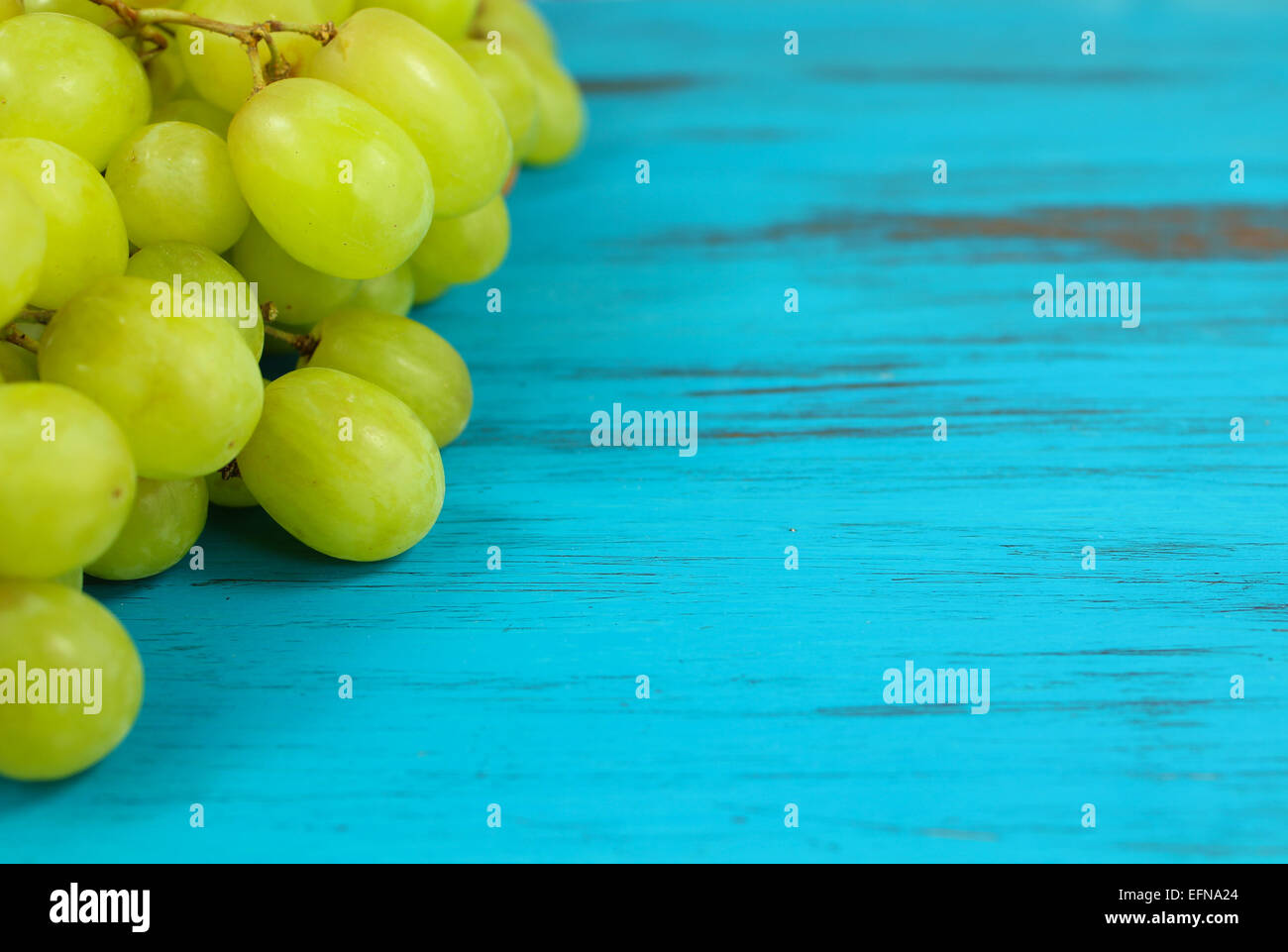 Close up di Bright Green uve su un turchese distressed sfondo di legno Foto Stock