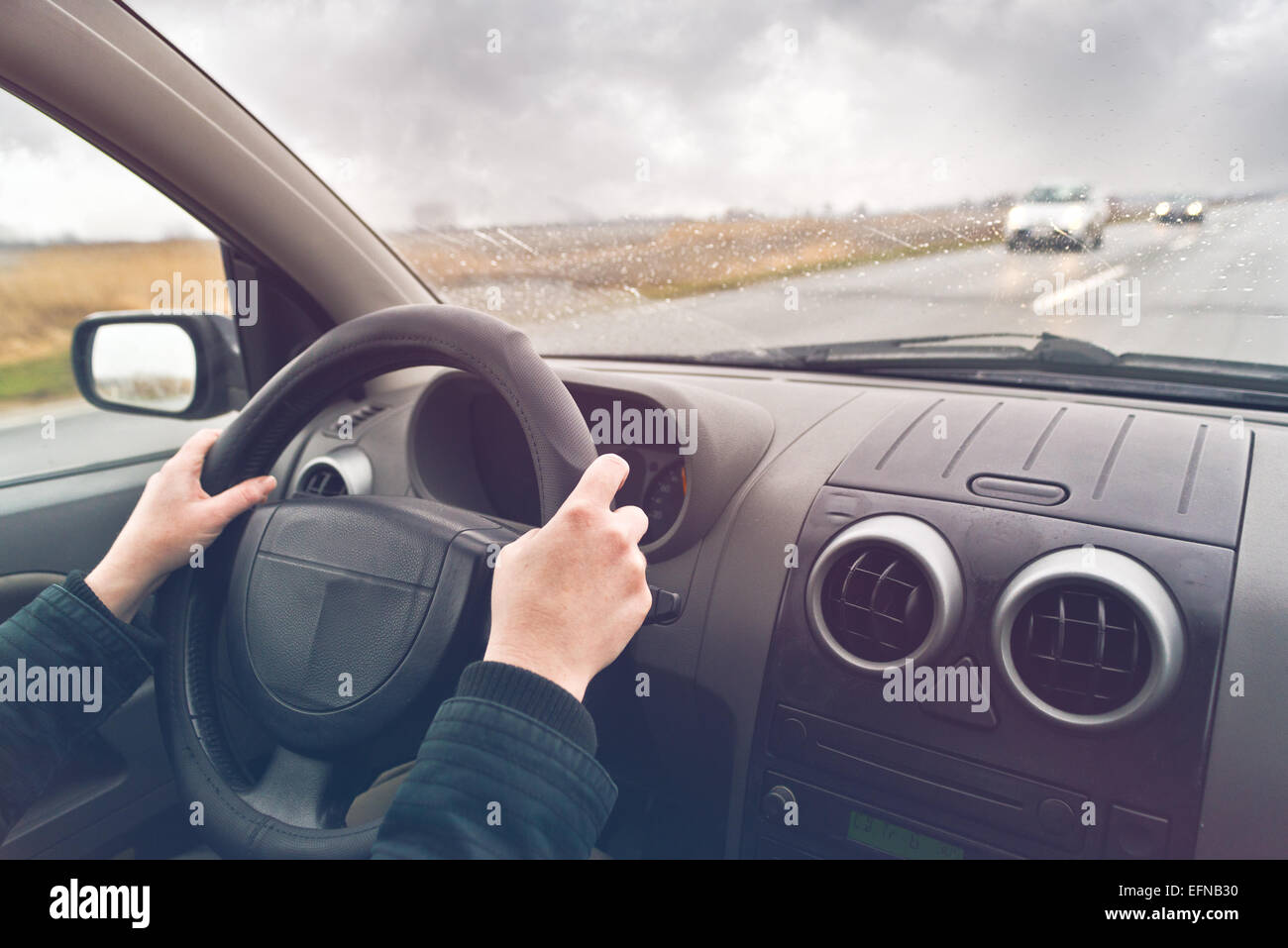 Le mani di una femmina di guidatore sul volante di un veicolo in un nuvoloso giorno d'inverno. Foto Stock