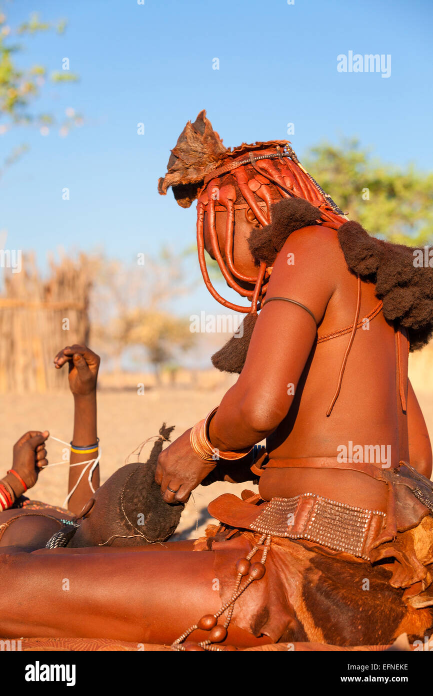 Una donna Himba rendendo trecce tradizionali su una giovane ragazza, Namibia. Foto Stock