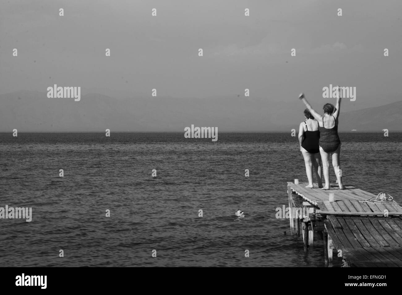 Foto in bianco e nero di due signore felice sui costumi da bagno in un molo in legno momenti prima di saltare nell'acqua. Foto Stock