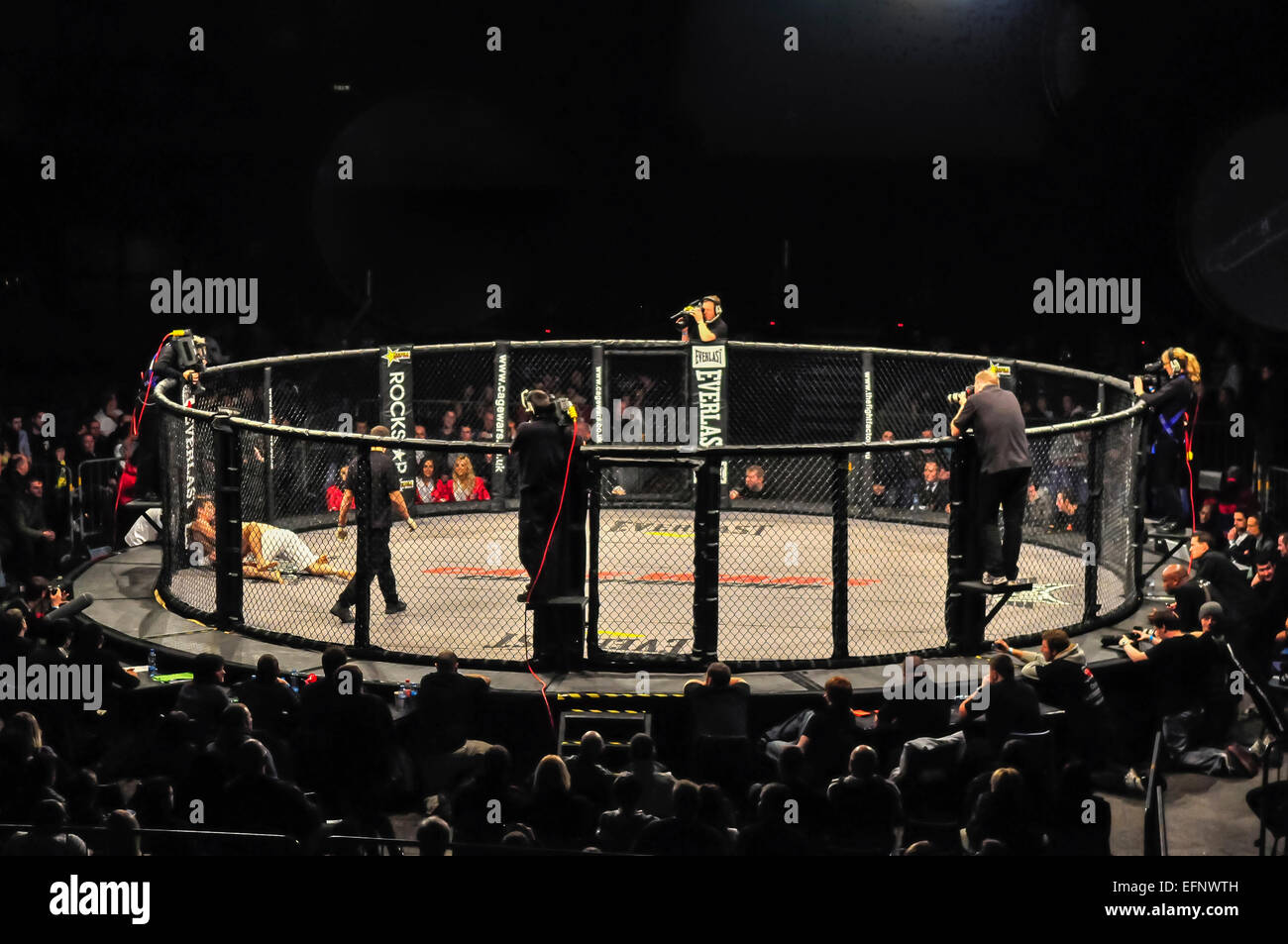 Pubblico e telecamere guarda su come due avversari di lotta in una gabbia MMA lotta Foto Stock