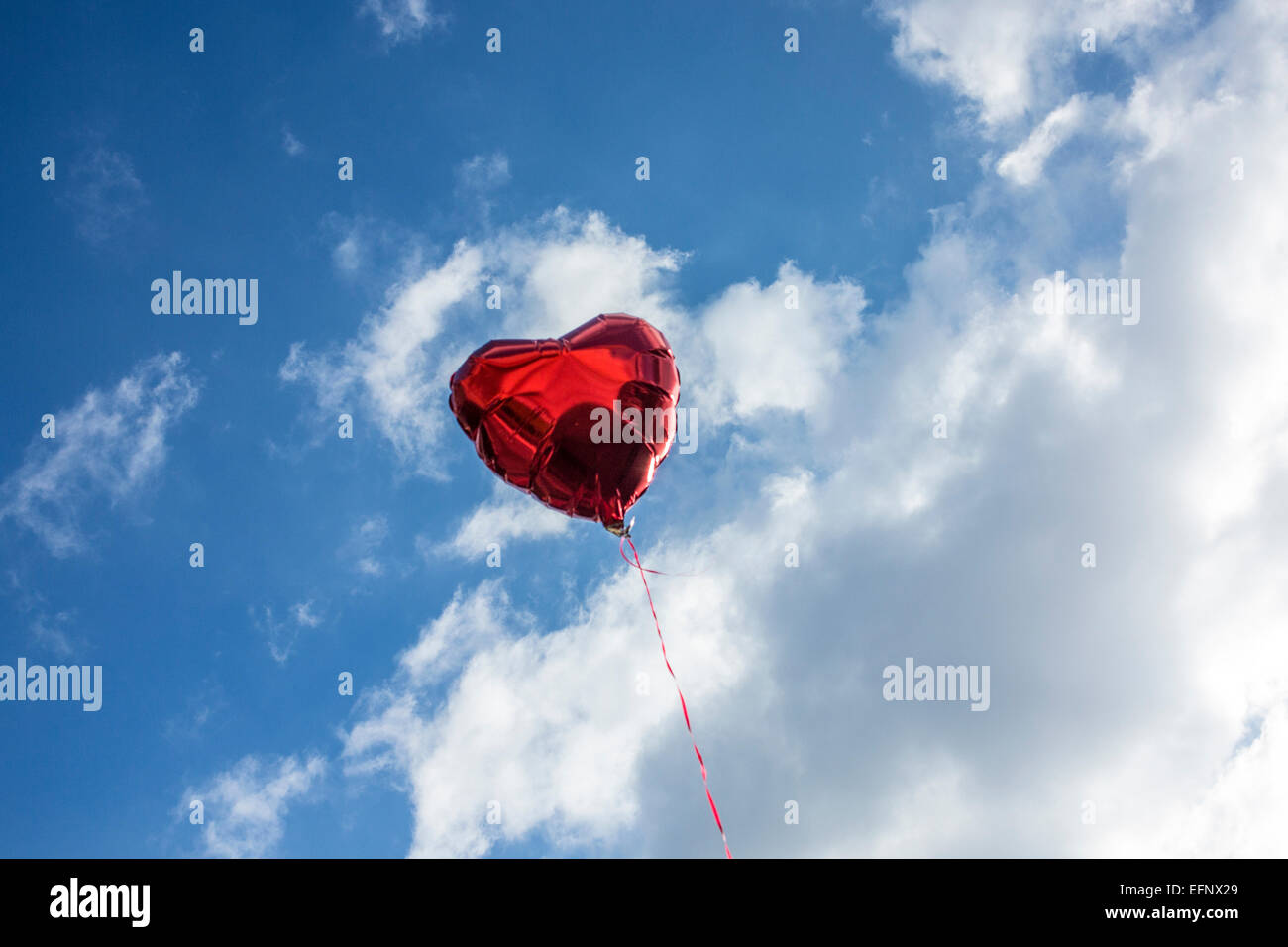 Un cuore rosso a forma di palloncino elio in un blu cielo nuvoloso Foto Stock