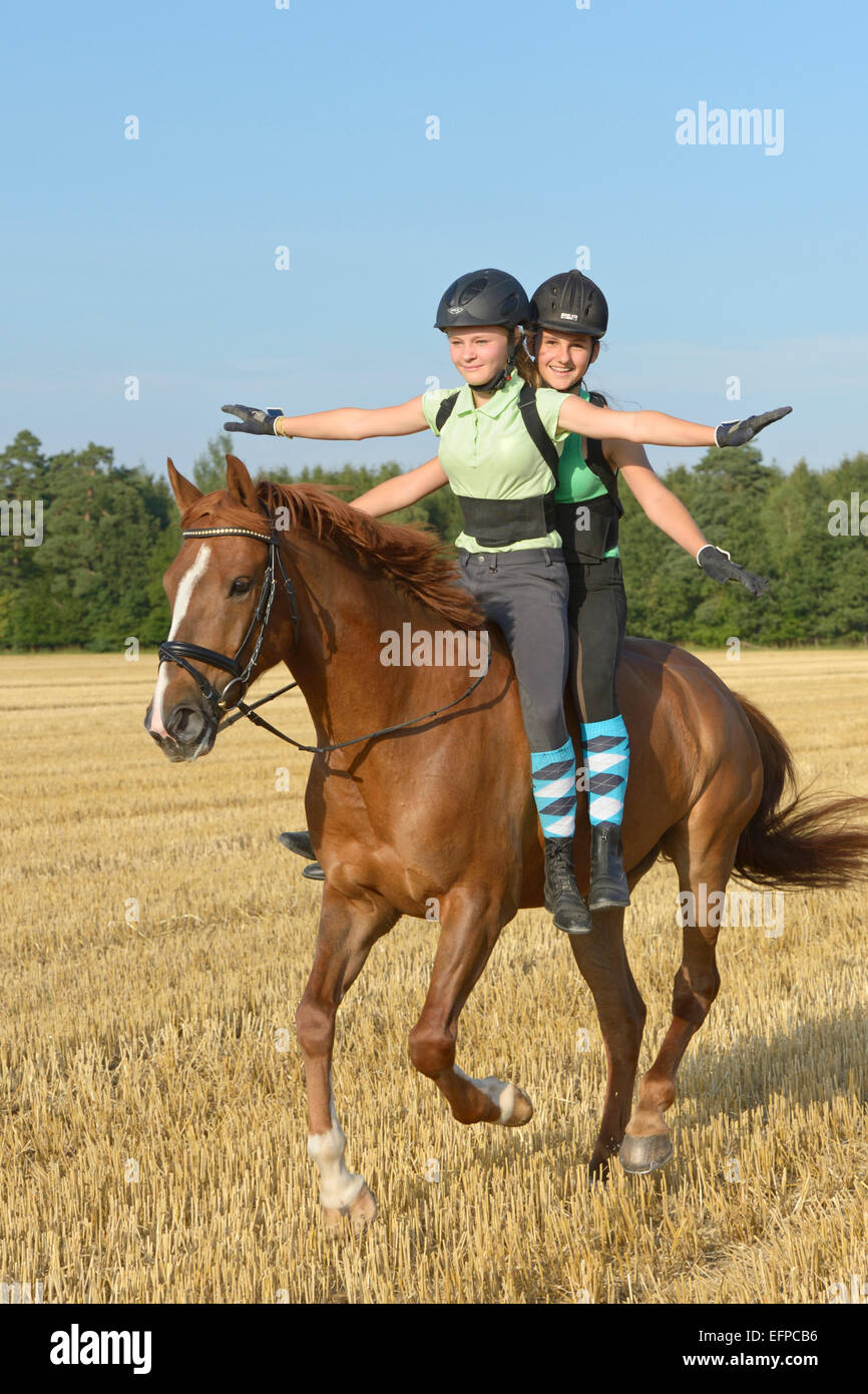 Due giovani ragazze che indossano il casco di protezione posteriore insieme a cavallo di freehand assieme back Sport irlandesi Pony cavallo al galoppo campo di stoppie Germania Foto Stock